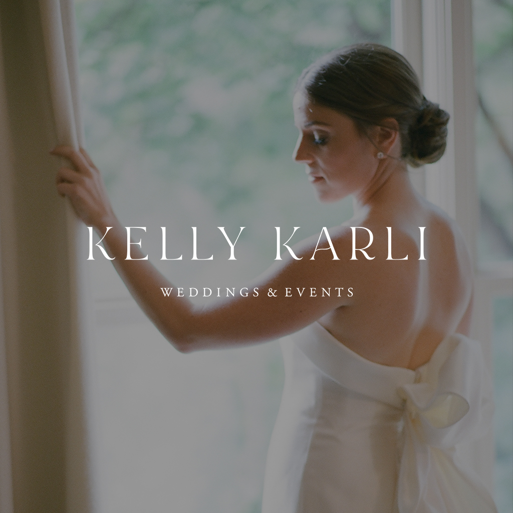 A bride looks out a window. Her hair is up in a low bun, and she wears an off the shoulder dress. Kelly Karli Weddings & Events logo overlays the image.